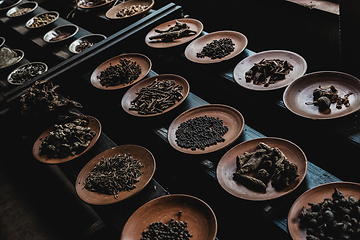 Image showing Various spices displaied on small ceramic and metal plates on black wooden background.