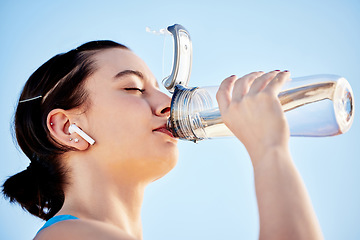 Image showing Drinking water, fitness and music with a sports woman hydrating during a run on a blue sky background outdoor. Wellness, health and exercise with a female runner or athlete taking a drink to hydrate