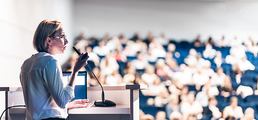 Image showing Female speaker giving a talk on corporate business conference. Unrecognizable people in audience at conference hall. Business and Entrepreneurship event.