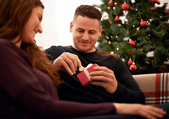 Image showing Christmas, present and couple on a sofa for gift exchange, bond and relax while celebrating in a living room. Box, present and love by man and woman on a couch for festive, xmas and traditional day