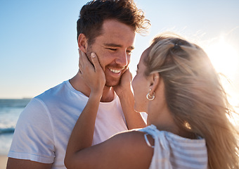 Image showing Woman, man and touch face, love and happy together at the beach, travel and romance outdoor for bonding. Couple on adventure by the ocean, embrace with lens flare and care while spending quality time