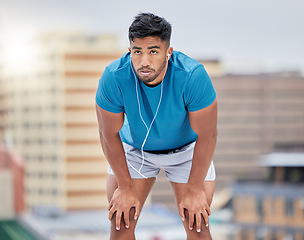 Image showing Man, tired and running in city for exercise, workout or training by blurred background, buildings and breathing. Runner, relax or rest to music, streaming or outdoor for fitness, health and wellness