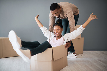 Image showing Couple, box and moving into real estate, home and fun while unpacking, playing and bond in a living room. House, fun and man with woman on a floor playful, laughing and celebrating their dream home