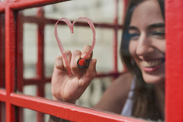 Image showing Woman, heart and drawing with lipstick in booth for love on travel vacation in London city. Happy, red cosmetics makeup and person graffiti on window for freedom, pop art and adventure holiday