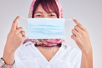 Image showing Covid, mask and safety with a muslim woman in studio on a gray background for a new normal lifestyle. Compliance, health and safe with an islamic female show how to wear a face mask during pandemic