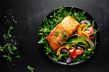 Image showing Salmon fillet grilled and fresh vegetable green salad of arugula with tomatoes, olives and bell pepper on black background, healthy food, mediterranean diet, top view