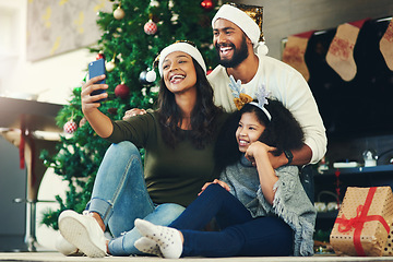 Image showing Selfie, family and christmas with a mother, father and daughter sitting for a photograph at home with a gift by a tree. Kids, fun and love with a girl, woman and man posing for a festive picture