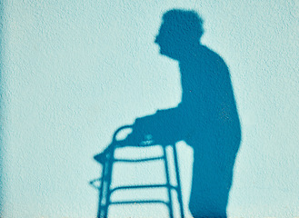 Image showing Shadow, disability and walking with a senior woman outdoor on a blue wall background on a sunny summer day. Silhouette, handicap and mobility walker with a mature female outside alone for a walk