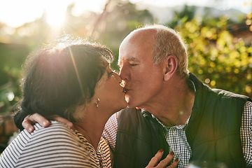 Image showing Kiss, love and senior couple in nature for love, date and affection during retirement holiday. Happy, care and interracial man and woman kissing with an embrace and smile in a park or garden