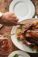 Image showing Hands, food and carving the turkey with a senior man using a knife at a dining room table in his home. Chicken, thanksgiving and tradition with a mature male cutting meat during a roast meal or feast