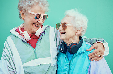 Image showing Happy, fashion and elderly friends hug in cool sunglasses, vintage jackets and modern headphones outdoors. Retro, wall background and senior women hugging with pride, freedom and smile in retirement