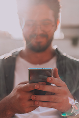 Image showing A young man utilizes his smartphone outdoors, showcasing the seamless integration of technology and mobility in modern professional life.