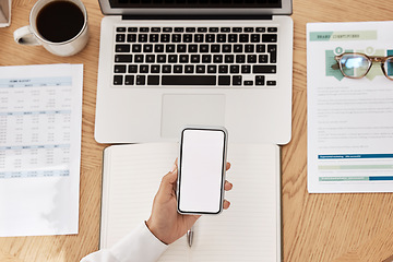 Image showing Laptop, paperwork and phone with mockup space at a desk in a modern office working on project. Cup of coffee, computer and hand holding a smartphone with blank screen with copy space in the workplace