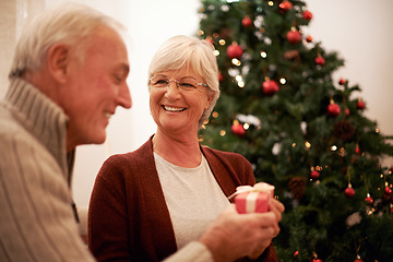 Image showing Senior couple, giving gift and together for Christmas holiday celebration at home with a smile, happiness and kindness. Surprise, celebrate and tree with man and woman holding a present and gift box
