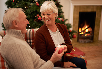 Image showing Christmas, gift and love with a senior couple in celebration while sitting in the living room of their home together. Tradition, present and bonding with a mature man and woman in the festive season