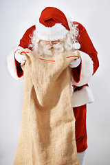 Image showing Santa Claus, bag and gift with a man in a costume posing in studio on a gray background for the holidays. Delivery, Father Christmas and sack with a male in an outfit for festive season celebration