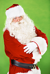 Image showing Christmas, santa and costume with a man in studio on a green background for festive season celebration. Portrait, glasses and serious attitude of saint nick standing arms crossed for the holidays