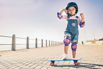 Image showing Children, skate and strong with a girl on her skateboard for fun on the beach promenade alone during summer. Muscle, bicep and helmet with a female child skating outside on a sidewalk with knee pads