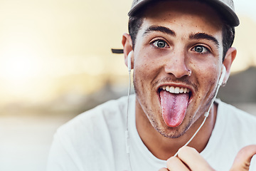 Image showing Fashion, city and portrait man with tongue out enjoy weekend, summer vacation and holiday. Freedom, comic and young male with funny face expression listening to music, radio and audio in urban town