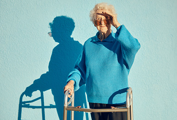 Image showing Portrait, shadow and disability with a senior woman on a blue wall background while holding a mobility walker outdoor. Health, handicap and fashion with a mature female standing outside alone