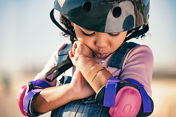 Image showing Children, skater and plaster with an injured girl looking at her sore arm while skating outdoor in a helmet and pads. Training, safety and injury with a female kid in pain after a sports accident