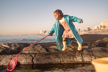 Image showing Children, beach and fishing with a girl using a net in a rock pool while having fun on summer vacation. Water, nature and kids with a black child outdoor by a tide pool to fish and enjoy her holiday