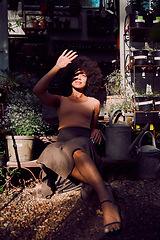 Image showing Sun, shadow and light with beauty woman, garden and relax during summer, happy smile and afro in backyard outdoor. Latino female, fashion and relaxing in sunlight, gardening shed and pot plants