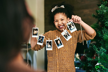 Image showing Girl, photo string or hanging on christmas tree, family home or decoration in holiday happiness. Child, pictures or interior design for celebration, party or event in house with smile, art and tree