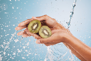 Image showing Water splash, hands of woman and kiwi in studio on a blue background. Cleaning, hygiene and female model washing fruits for healthy diet, nutrition and vitamin c for skincare, beauty and wellness.