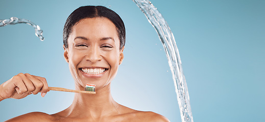 Image showing Black woman, toothbrush and brushing teeth with a water splash and toothpaste on blue studio background for dental health and wellness. Portrait and face of model cleaning mouth with eco brush