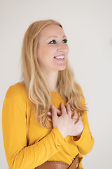 Image showing Portrait of cheerful confident beautiful woman with long blond hair, wearing casual clothes, standing in relaxed pose with hands on chest, breathing deeply, doing breathing exercise