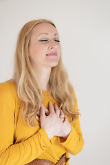 Image showing Portrait of cheerful confident beautiful woman with long blond hair, wearing casual clothes, standing in relaxed pose with hands on chest, breathing deeply, doing breathing exercise