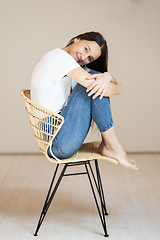 Image showing Portrait of confident beautiful woman with long brown hair, wearing casual clothes, sitting on chair in tight jeans and white t-shirt, studio background