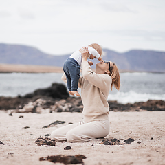 Image showing Mother enjoying winter vacations holding, playing and lifting his infant baby boy son high in the air on sandy beach on Lanzarote island, Spain. Family travel and vacations concept