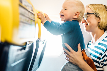 Image showing Mom and child flying by plane. Mother holding and playing with her infant baby boy child in her lap during economy comercial flight. Concept photo of air travel with baby. Real people.