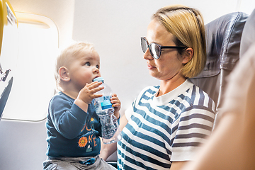 Image showing Mom and child flying by plane. Mother holding and playing with her infant baby boy child in her lap during economy comercial flight. Concept photo of air travel with baby. Real people.