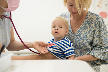 Image showing Infant baby boy child being examined by his pediatrician doctor during a standard medical checkup in presence and comfort of his mother. National public health and childs care care koncept.