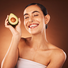 Image showing Face, skincare and avocado with a model woman in studio on a brown background to promote healthy eating. Food, health and wellness with an attractive young female inside for luxury or natural care