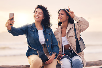 Image showing Selfie, peace sign and women with phone, beach and relax outdoor for fun, travel and smile together. Female friends, young girls and sunset with smartphone, hand gesture and social media to connect.
