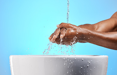 Image showing Clean, water and man washing his hands for hygiene, to stop germs and prevent bacteria in a studio. Wellness, health and closeup of a guy cleaning his hand by a basin isolated by a blue background.