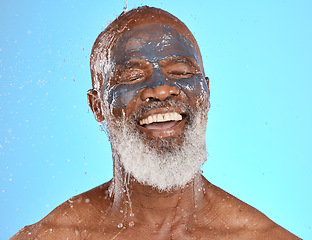 Image showing Face, water splash and senior black man in clay mask in studio isolated on a blue background. Cleaning, retired and elderly male from Nigeria washing off facial cosmetics for skincare or healthy skin