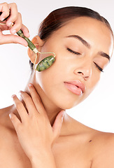 Image showing Face, beauty and skincare of woman with jade roller in studio isolated on a white background. Makeup, cosmetics and female model from Canada with eyes closed and facial roller for healthy smooth skin