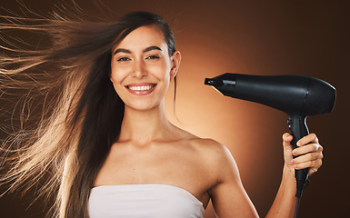 Image showing Beauty, hair and hairdryer with a model woman in studio on a brown background for blowdrying or treatment. Portrait, haircare and style with an attractive young female drying or styling her locks