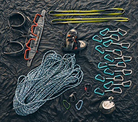 Image showing Rock or mountain climbing equipment or tools against dark background with a carabiner hook, rope for safety and security. Extreme sport object organized on floor or ground with sportswear and shoes