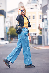 Image showing Portrait of fashion, beauty and cool woman with stylish sunglasses walking in a street in the city. Trendy blonde female looking carefree, hipster and confident while exploring urban town outdoor