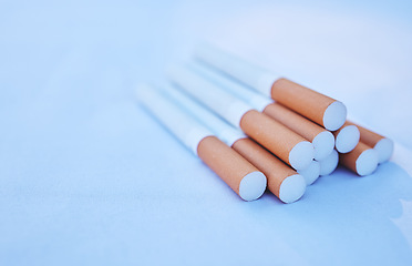 Image showing Cigarette, cancer and smoke with a tobacco product on the ground against a blue background to promote awareness. Smoking, toxic and addiction with cigarettes in a pile or stack on the floor