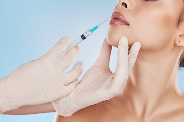 Image showing Lips, plastic surgery and filler with woman getting an injection with a syringe from the hands of a surgeon in gloves. Mouth, face and needle for beauty treatment in studio on a blue background.