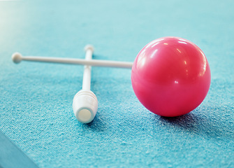 Image showing A red ball on the floor on a blue carpet with gymnastics club. Gym, fitness and training exercise equipment for rhythmic gymnastics isolated on blue background. Mockup for sports and dance athlete