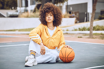 Image showing Young, fashionable and beautiful black woman basketball player or athlete with afro sitting on a court ground. Portrait of cool and edgy person in a sport outfit and funky fashion clothing outdoors