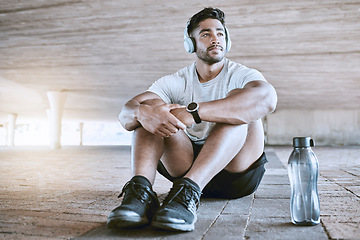 Image showing Athlete with headphones and water bottle on a relax break listening to music after his training exercise in the city with lens flare. Young sports man with audio fitness technology and workout gear